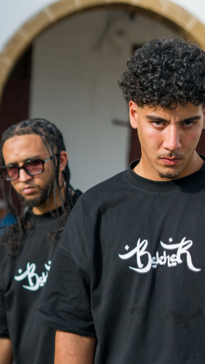 our-story Two young men pose wearing black t-shirts with logo design, outdoors in Morocco.