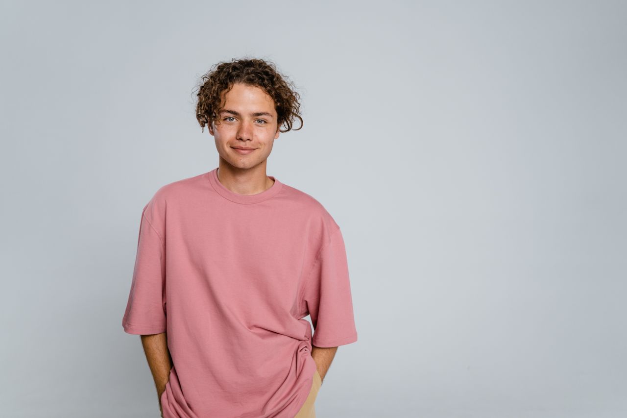 Smiling young adult wearing a pink t-shirt in a studio setting. Perfect for lifestyle or fashion themes.